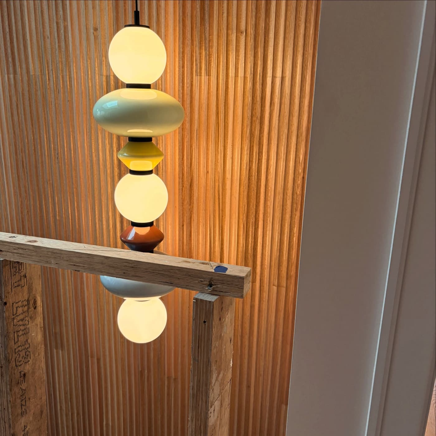A stacked glass bead pendant glowing against timber battens