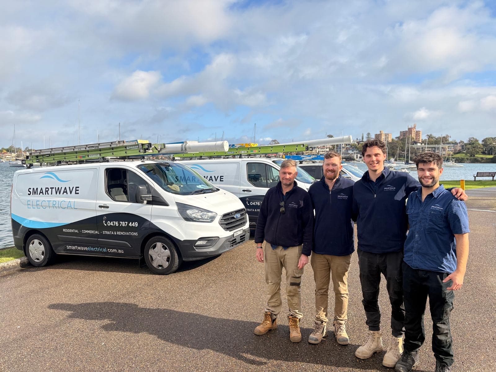 The Smartwave team in navy work gear, standing in front of three Smartwave vans by the harbour